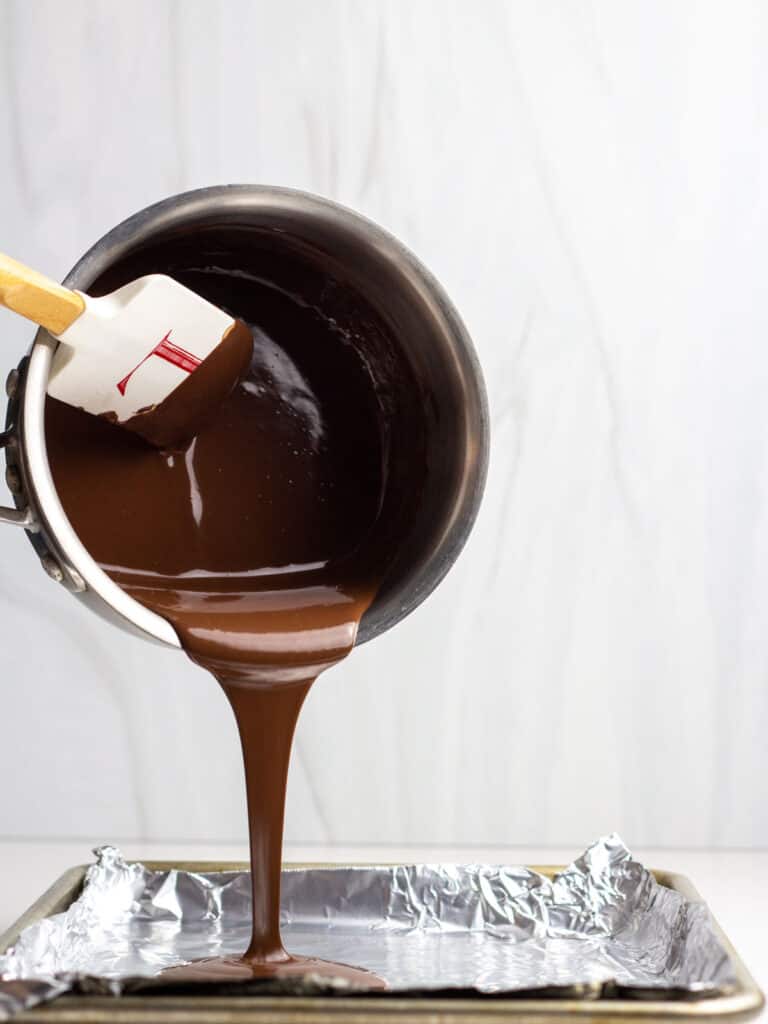 A spatula scraping chocolate out of a saucepan onto a foil lined baking sheet.
