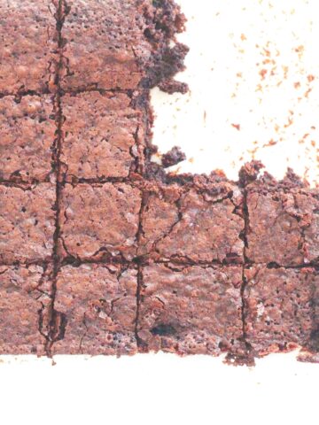 top down view of brownies on a white surface, still forming a large rectangle, however they have been cut in squares and 4 squares in the top right have been removed. The brownies go out of frame on the left side.