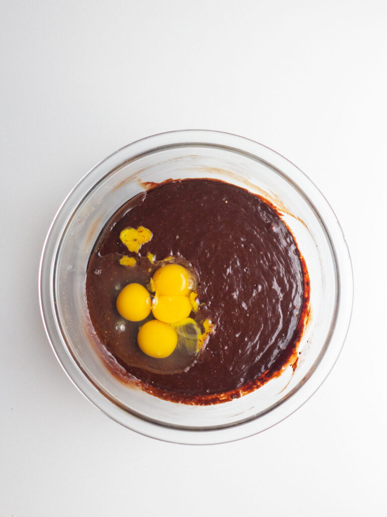 Clear glass mixing bowl with eggs and egg yolks added to the brownie batter.