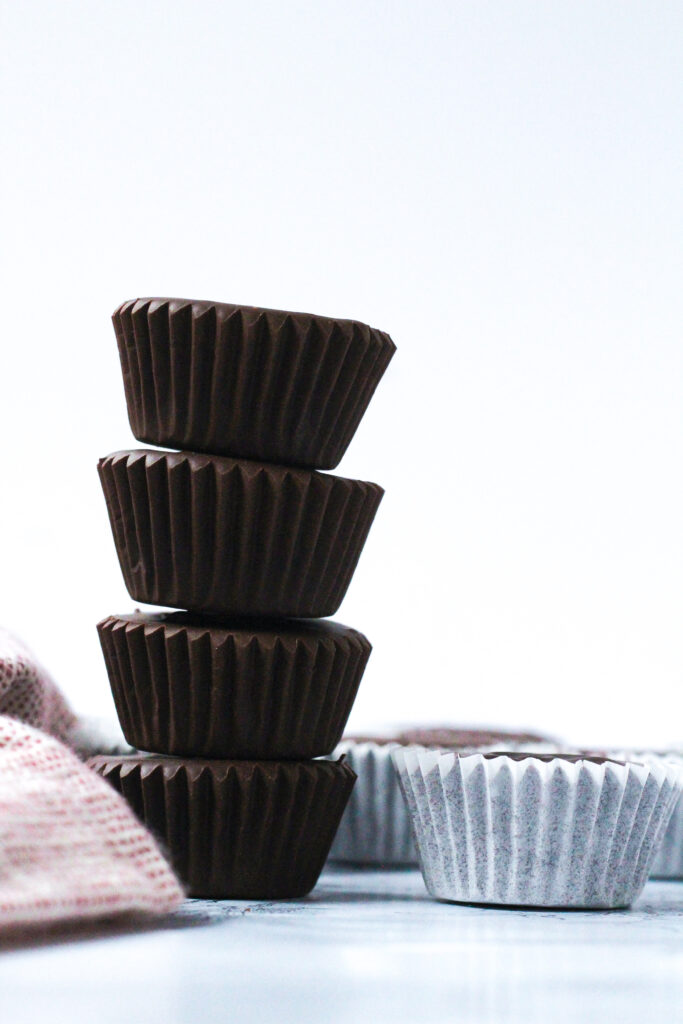 Side view of a stack of 4 dark chocolate peanut butter cups to the right of a red and white napkin. To the right of the stack are a single layer of peanut butter cups in white paper wrappers.