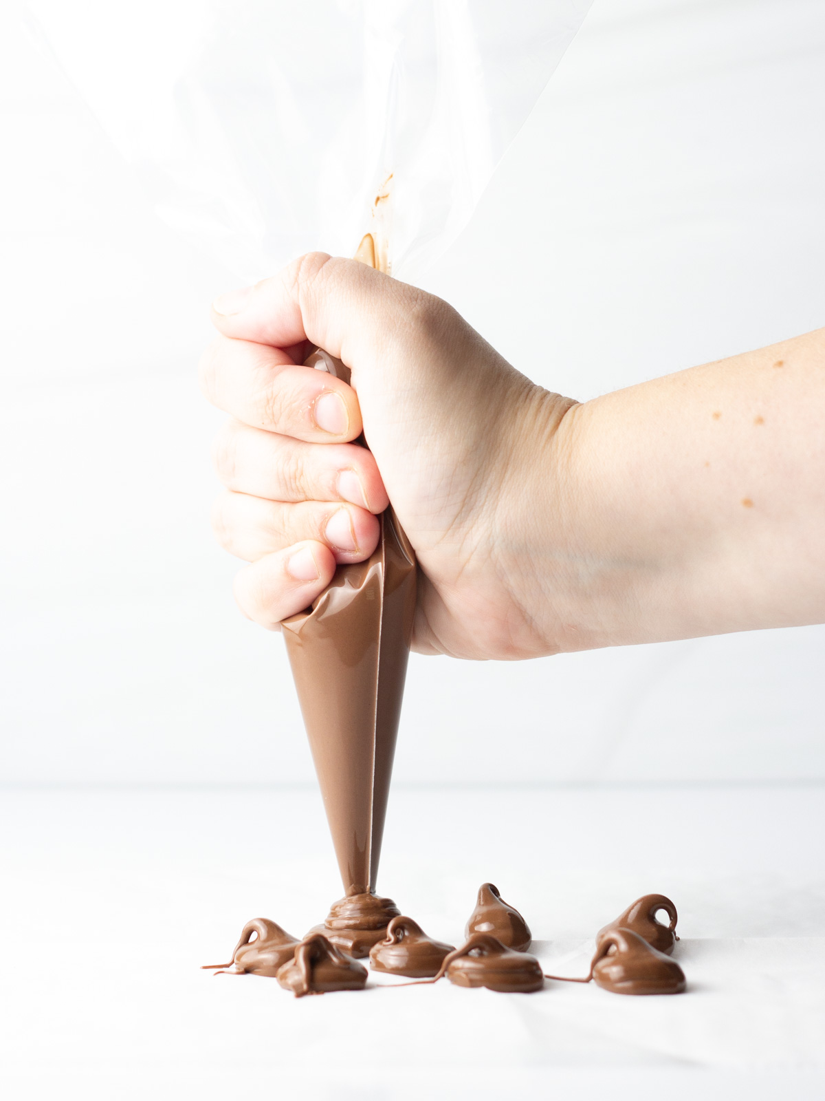 A hand holding a piping bag of Nutella piping dollops on to parchment paper.