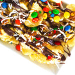 Salty sweet dessert nachos on a white plate topped with chocolate, caramel, m&ms, coconut, and sprinkles.