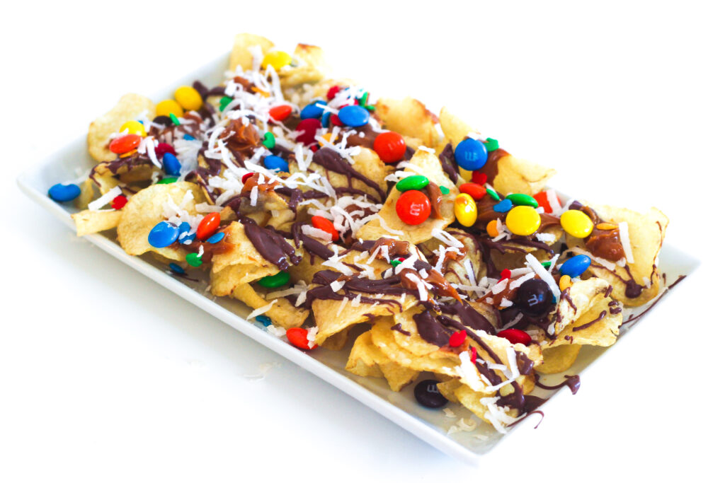 Easy no-bake dessert nachos loaded with chocolate, caramel, m&ms, coconut, sprinkles on rectangular white plate.