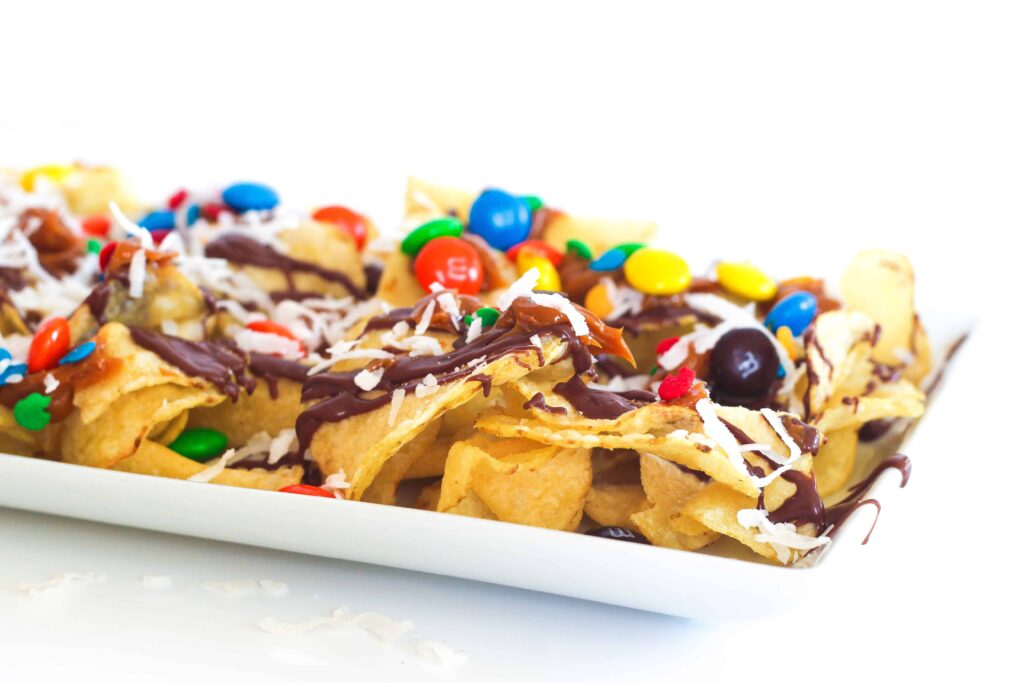 Salty sweet nachos loaded with chocolate, caramel, coconut, m&ms, and sprinkles on a rectangular white plate.