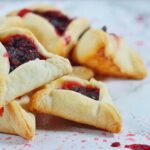 A pile of sangria hamentaschen sangria hamentashen on a white marble surface with spatters of filling on the marble