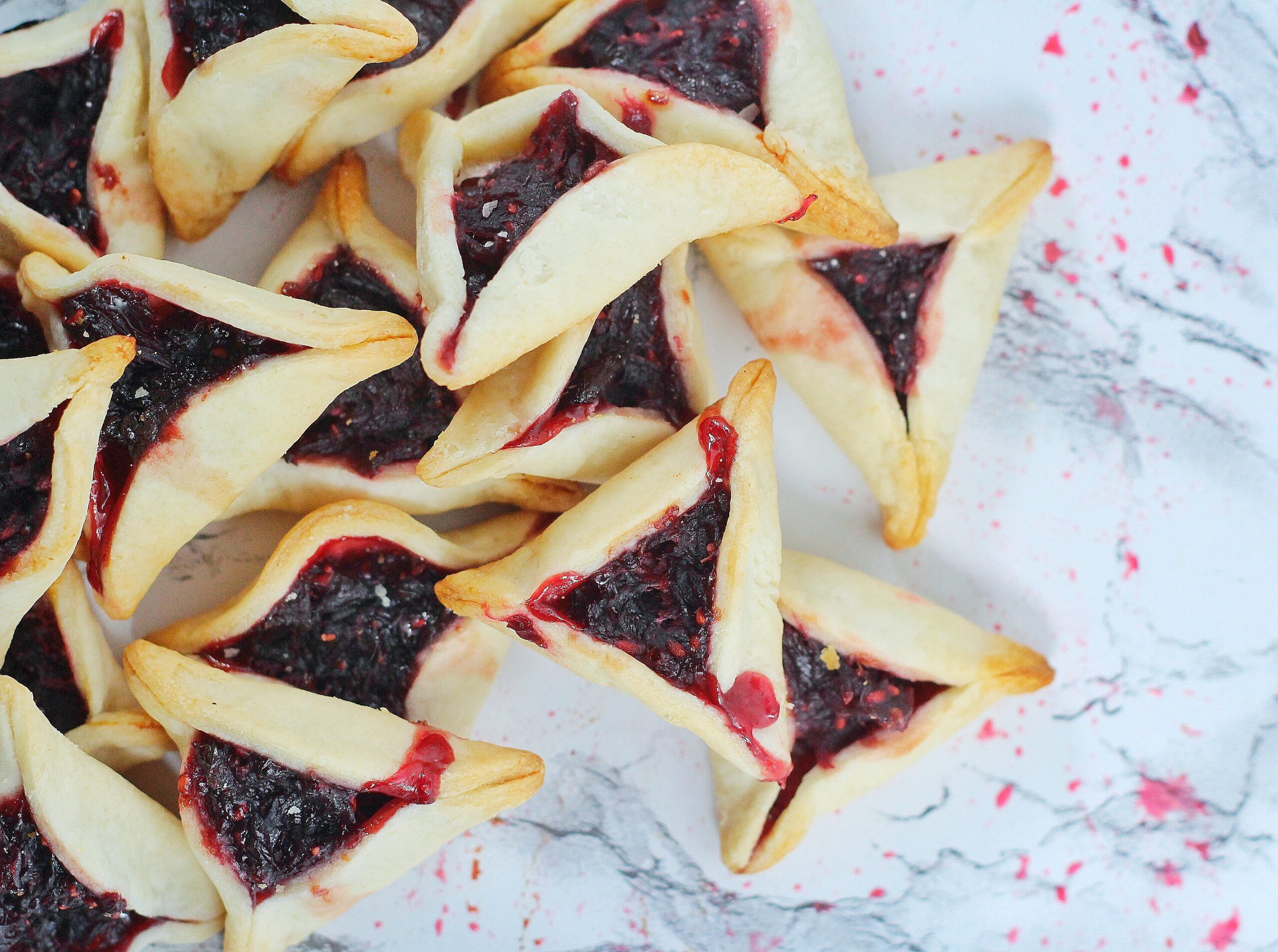 Overhead shot of sangria hamentaschen sangria hamentashen on a white marble surface with some splatters of filling on the marble
