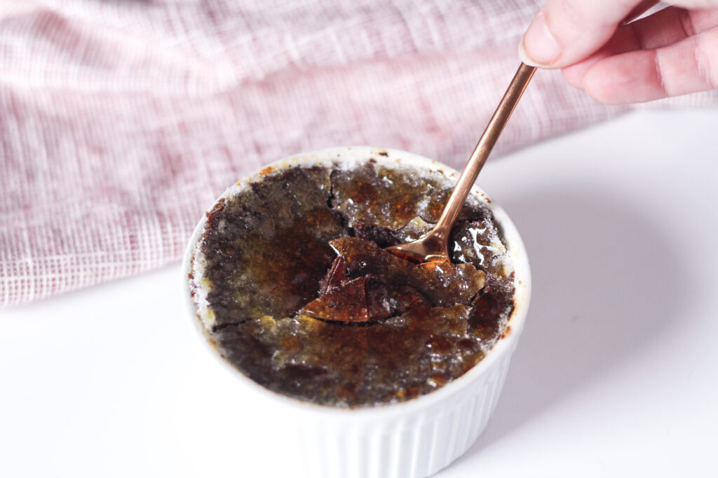 a spoon breaking through the crystalized topping of red wine chocolate creme brulee.