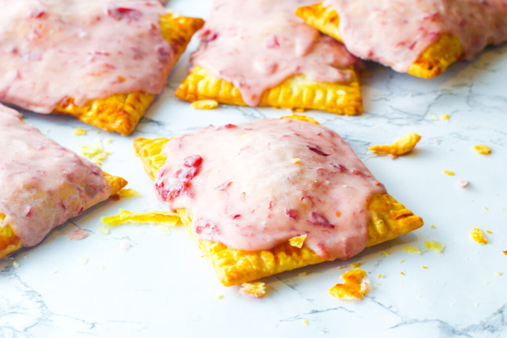 angled down view of sangria poptarts on a marbled surface surrounded by crumbs. One poptarts is focused in the center of the frame with more poptarts behind it at the top of the frame.