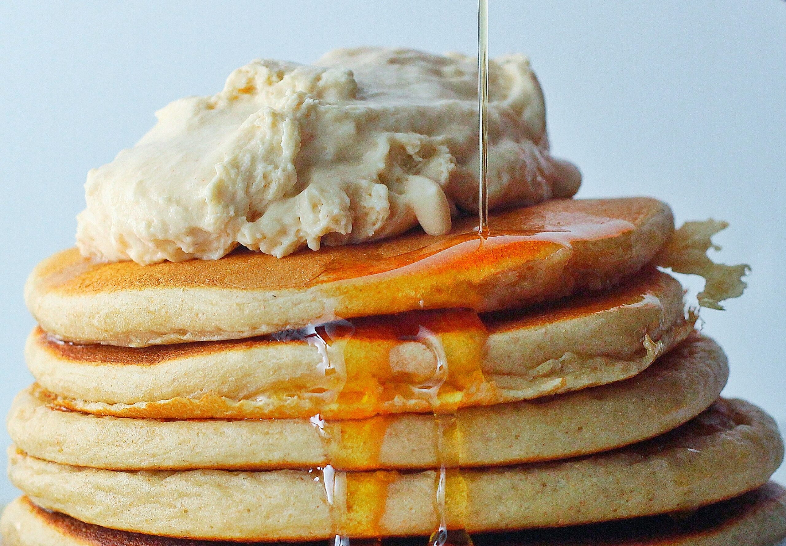 Whipped Peanut Butter piled on top of a stack of pancakes with a stream of maple syrup flowing down the side of the pancake stack