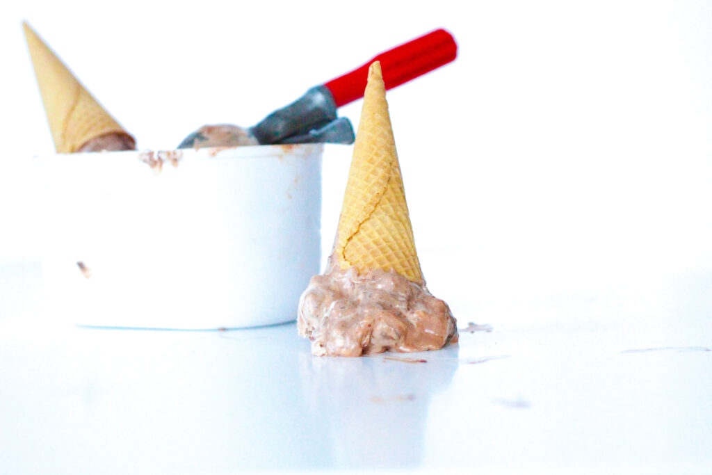 upside down cone of melting nutella ice cream in front of ice cream container and scoop.