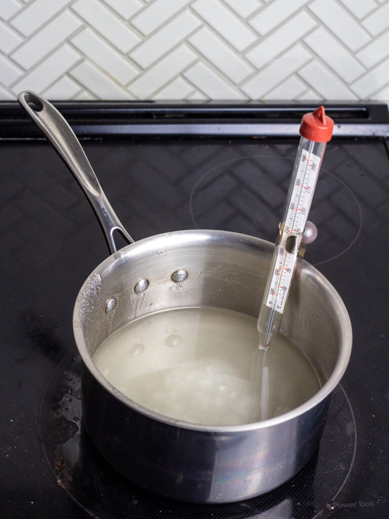 A saucepan on the stove with a candy thermometer clipped to the side.