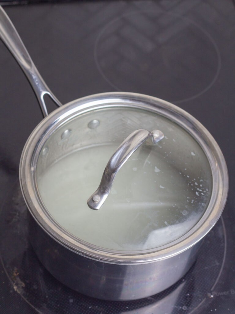 A covered sauce pan on the stove with corn syrup, sugar, and water inside.