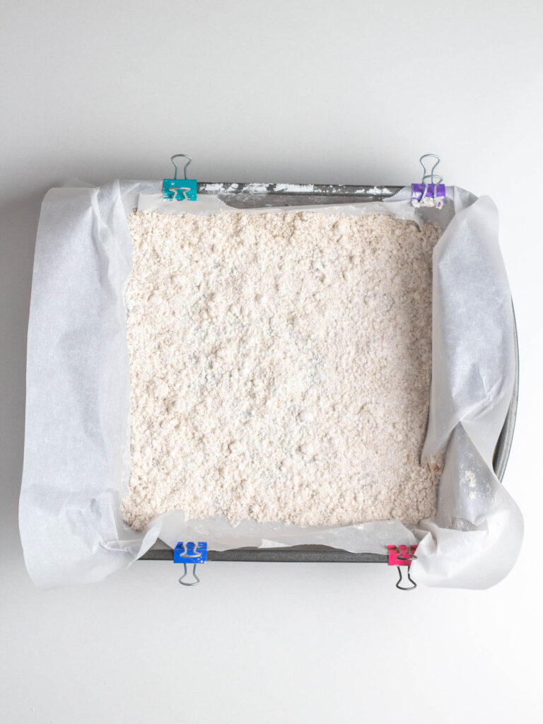 Square baking pan lined with parchment paper and covered with marshmallow coating mixture.