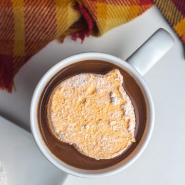 A pumpkin shaped pumpkin spice marshmallow floating in a cozy fall drink.