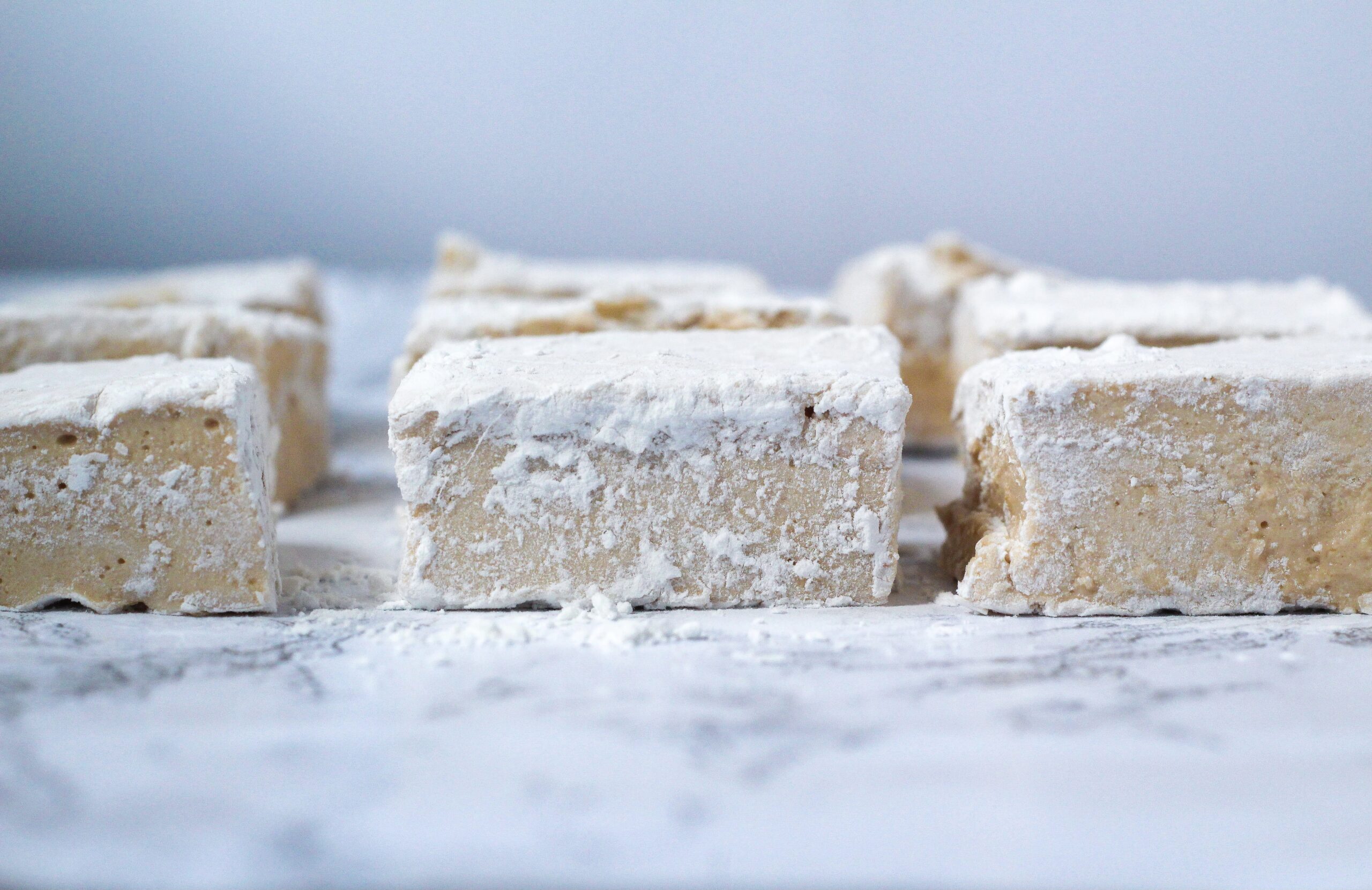 Side view of chai marshmallows lined up on top of a marbled surface in front of a white background