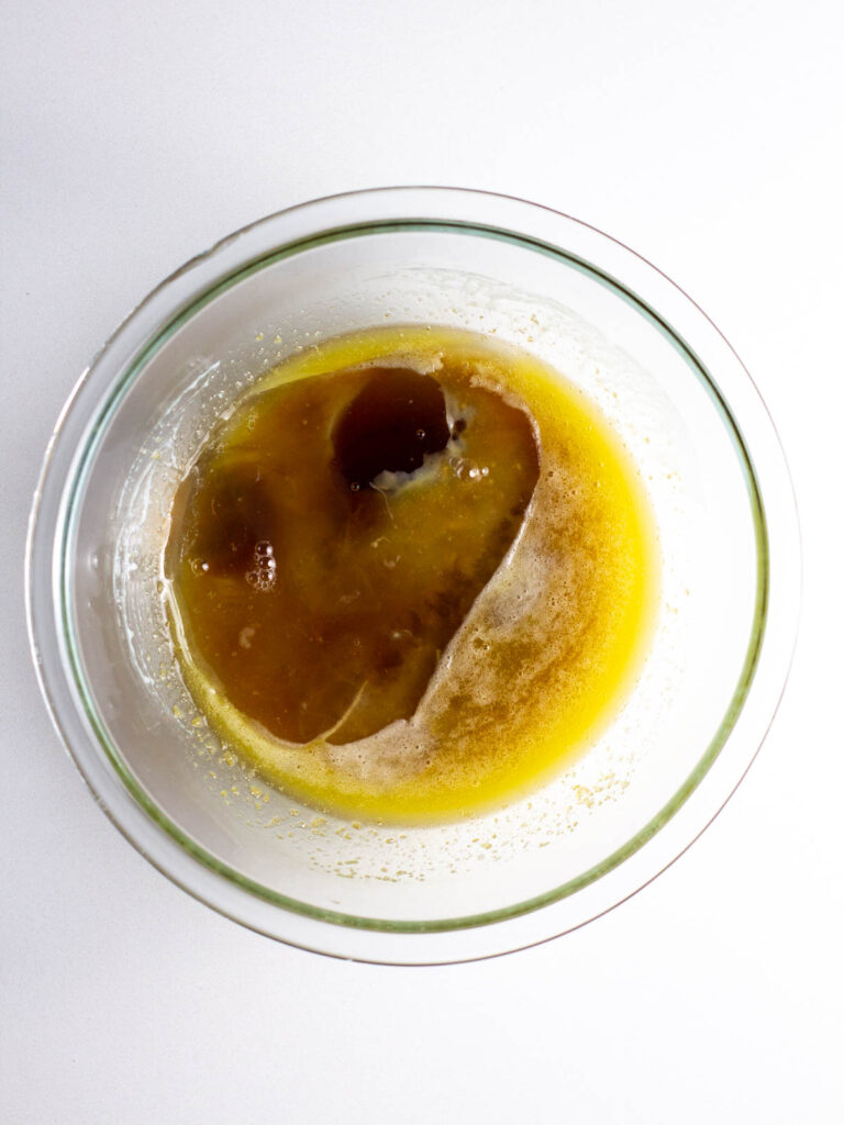 A clear glass bowl with maple syrup and an egg added to a melted butter and brown sugar mixture.