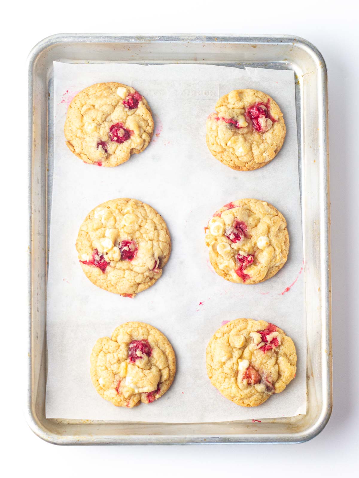 Top down view of baked cranberry white chocolate cookies on a parchment lined baking sheet.