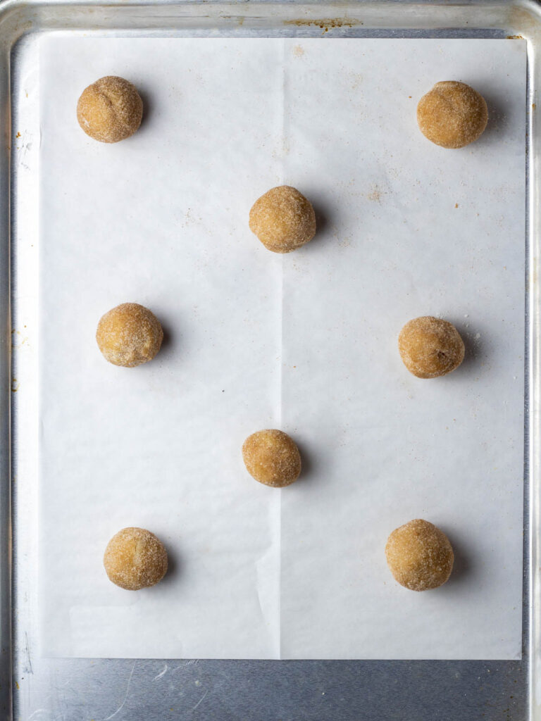 Balls of french toast cookie dough on a parchment lined baking sheet.