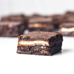 A peppermint mocha brownie in front of the rest of the batch of brownies showing the fudgy inside of the brownie with a layer of peppermint bark in the middle.