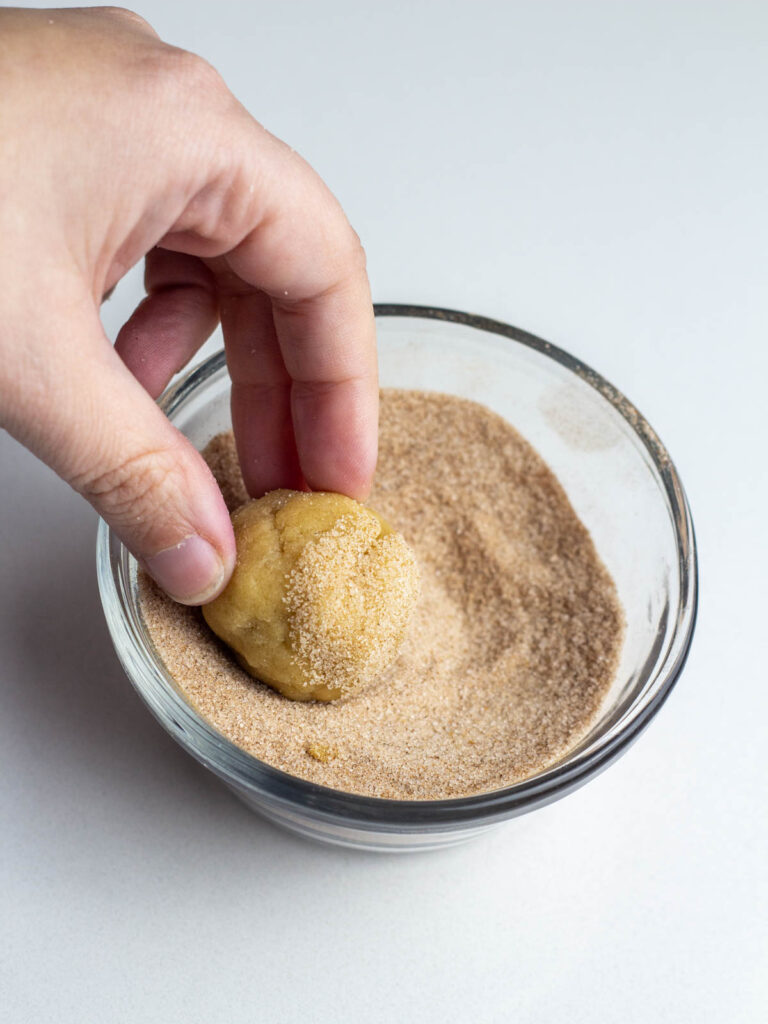 A cookie dough ball being rolled into a cinnamon sugar mixture.