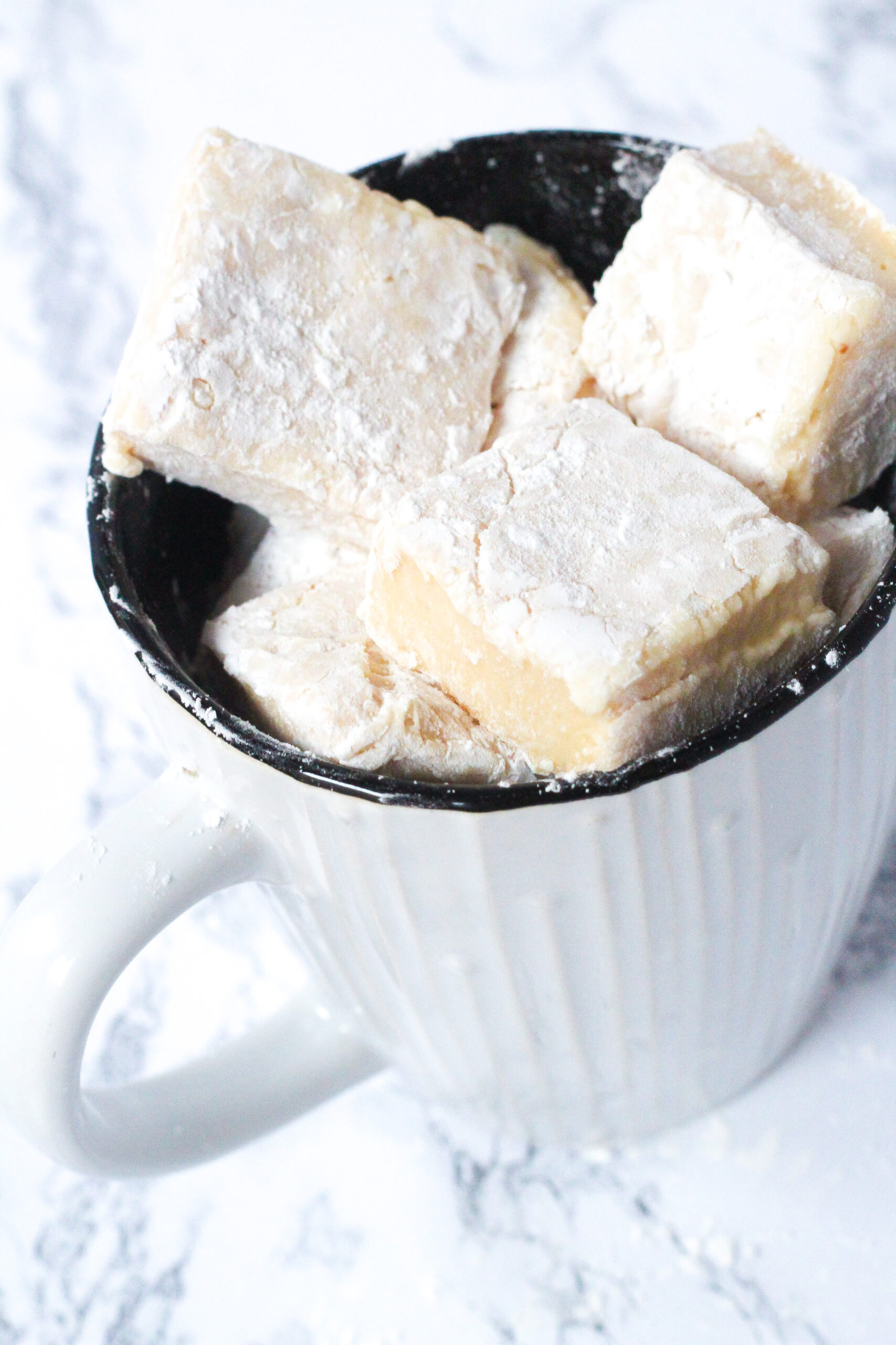 An angled top-down view of a mage that is white and textured on the outside and black on the inside, filled with Bailey's Marshmallows. The mug sits on a white marbled surface.