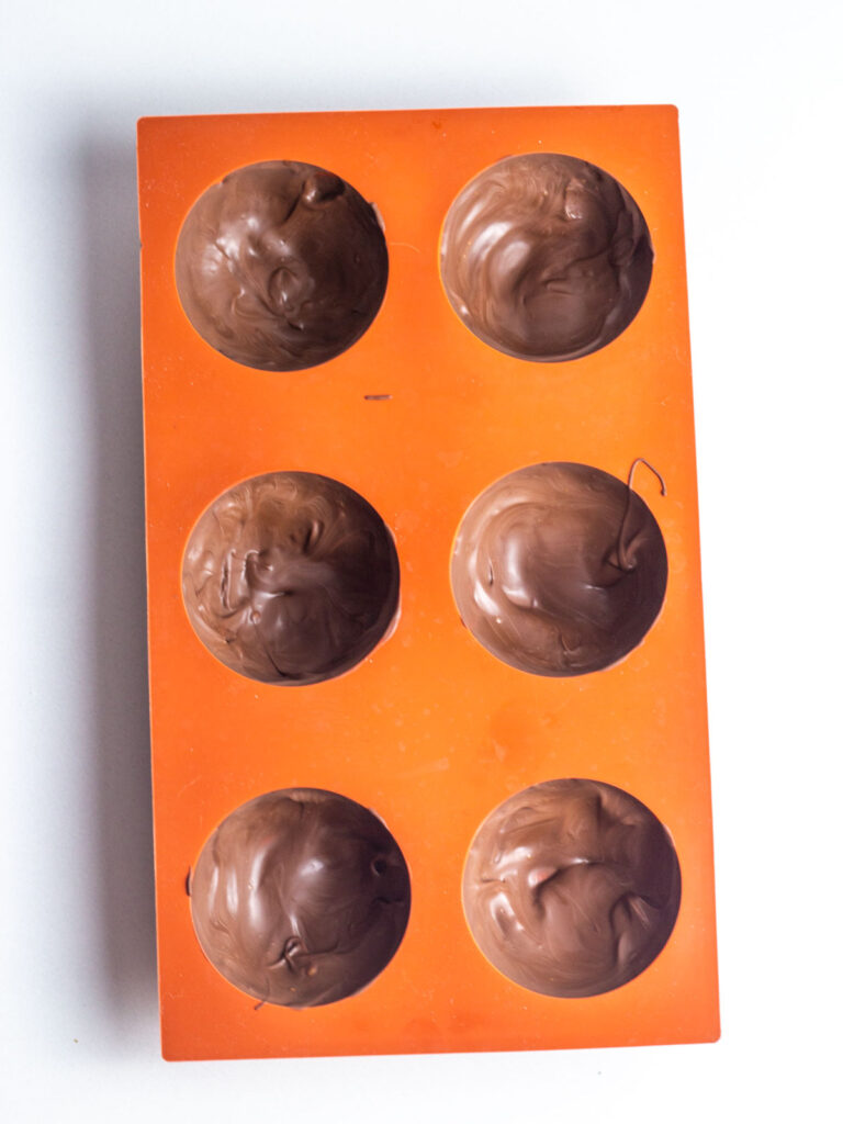 A red silicone half-sphere mold lined with a layer of chocolate.