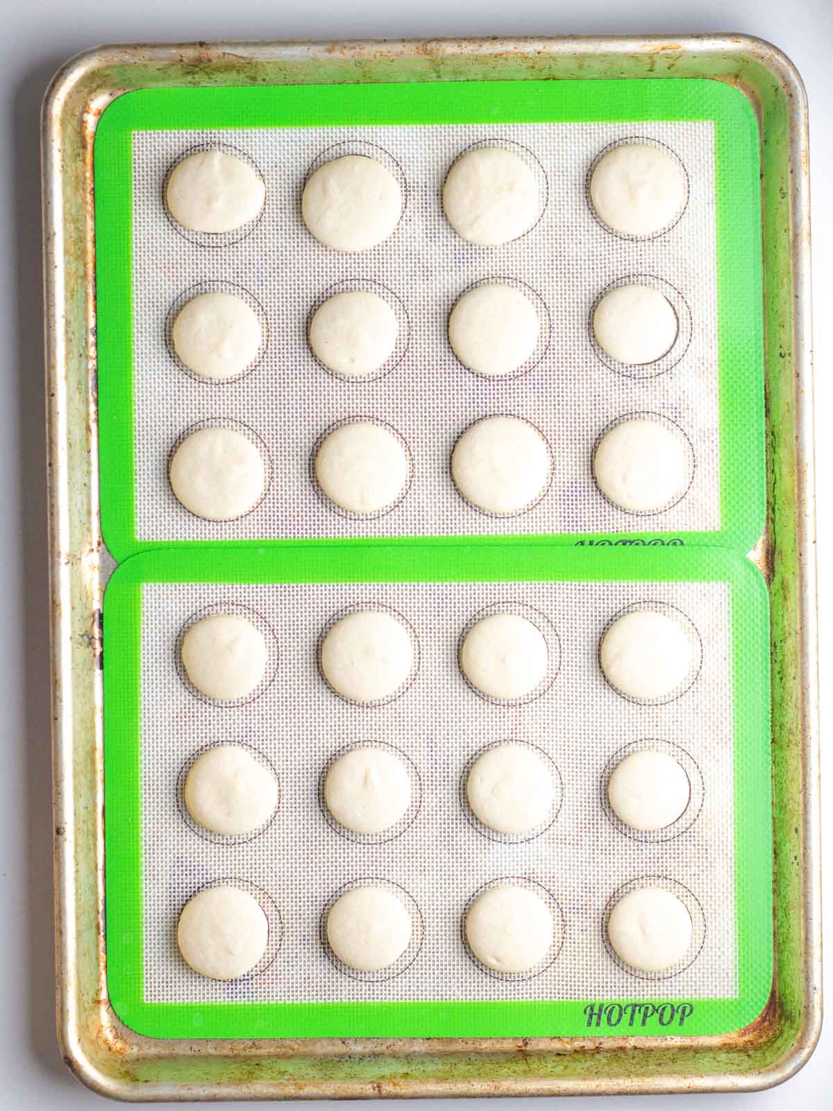 Two lined quarter baking sheets with baked macaron shells on silicone liners.
