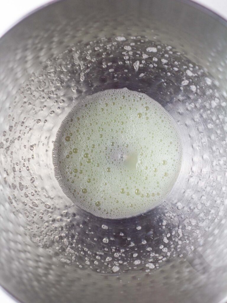 Foamy egg whites at the bottom of a textured silver metal mixing bowl.