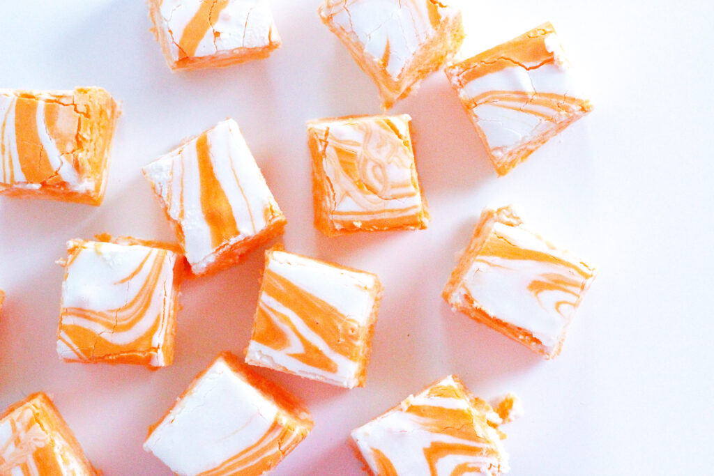 Top down view of creamsicle fudge - squares of swirled orange and white, sitting on a white surface.