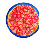 Top down view of a balsamic strawberry & basil tart on a blue plate on a white surface