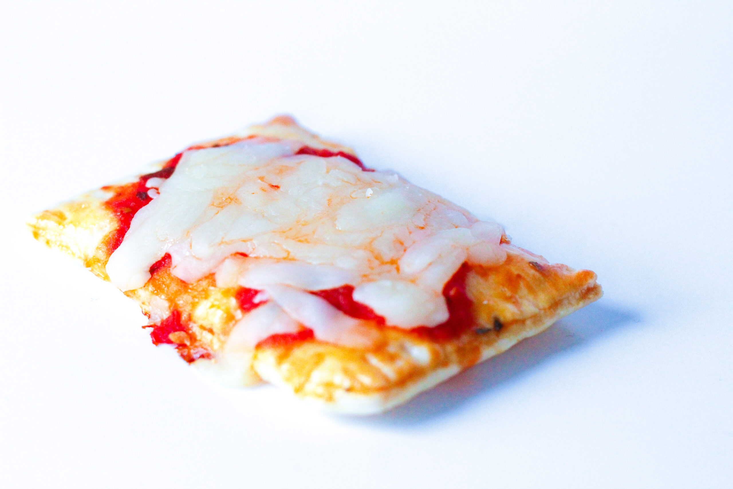 Close up of a pizza poptart on a white surface. A golden flakey crust with fork imprints around the edges, topped with red pizza sauce and white mozzerella cheese