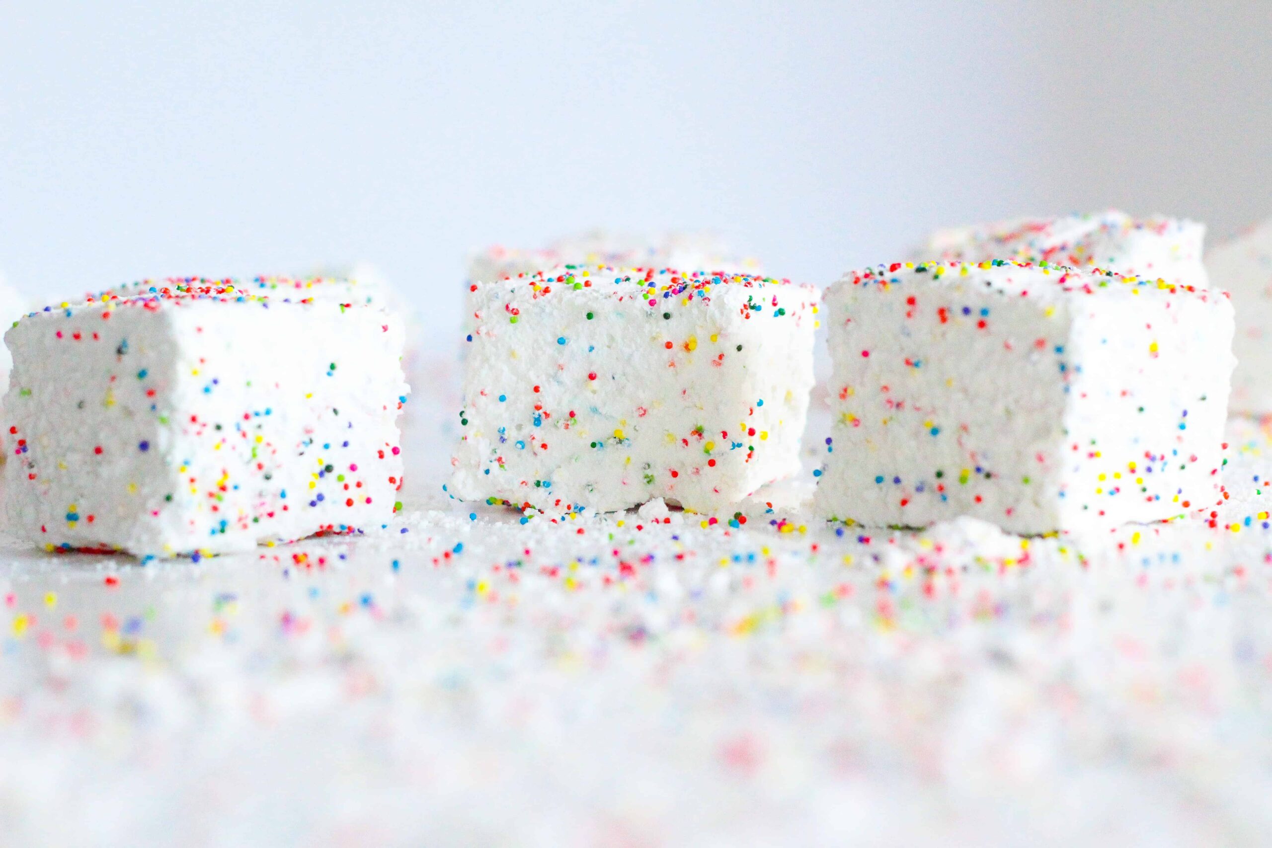 side view of three birthday marshmallows on a white surface with extra sprinkles everywhere