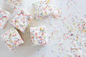 top down view of birthday marshmallows in the left hand side of the frame with excess cornstarch sprinkle coating on the right hand side of the frame. All on a white surface.