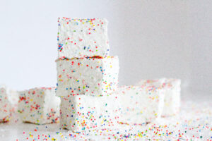 stack of 3 birthday marshmallows surrounded by other marshmallows and lots of sprinkles on a white surface