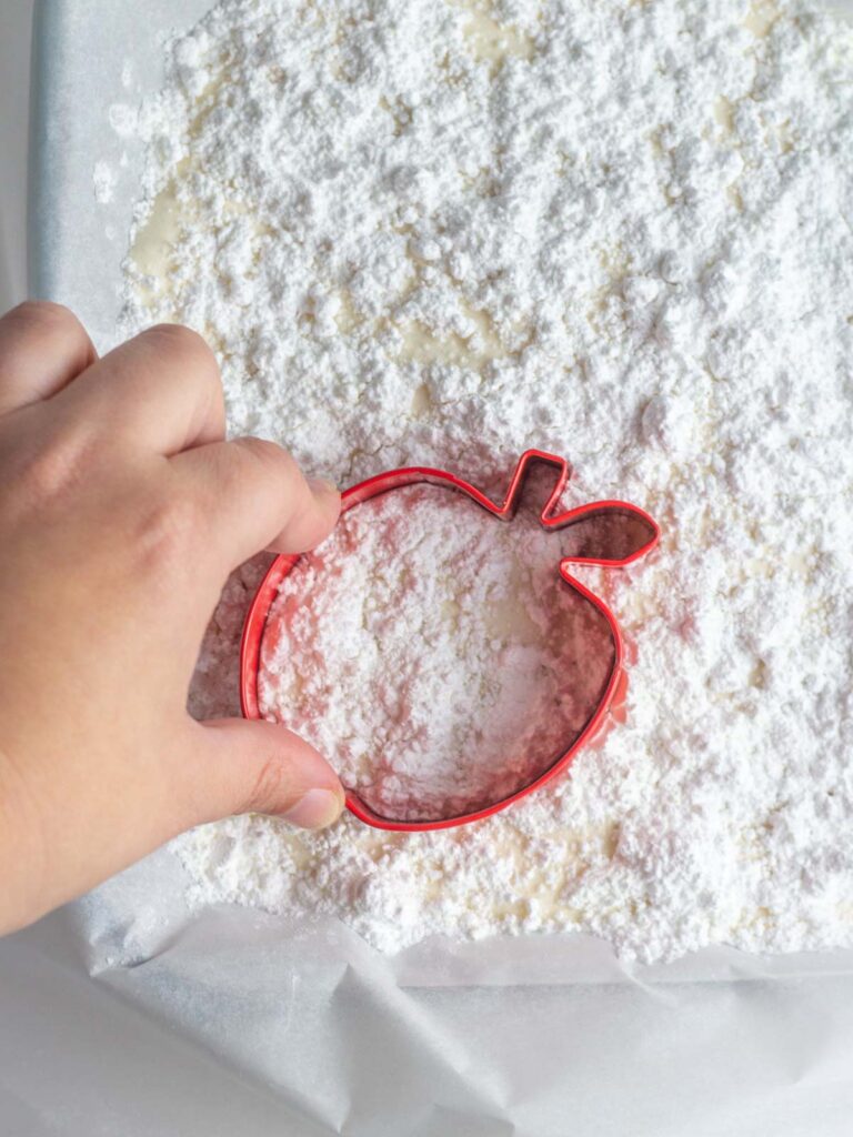 A hand pressing an apple shaped cookie cutter into pan of apple cider marshmallow.