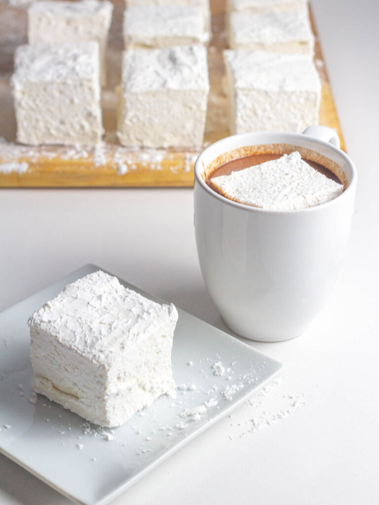 Apple Cider Marshmallow on a plate next to a mug with more marshmallows in the background.