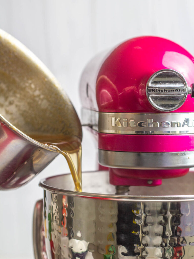 Pink Kitchenaid stand mixer with a saucepan streaming in the hot mixture.