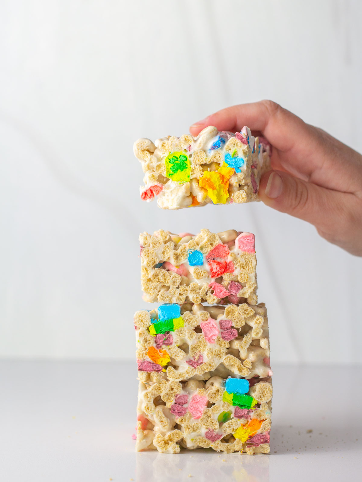 A hand placing a fourth lucky charms treat on a stack of three cereal bars.