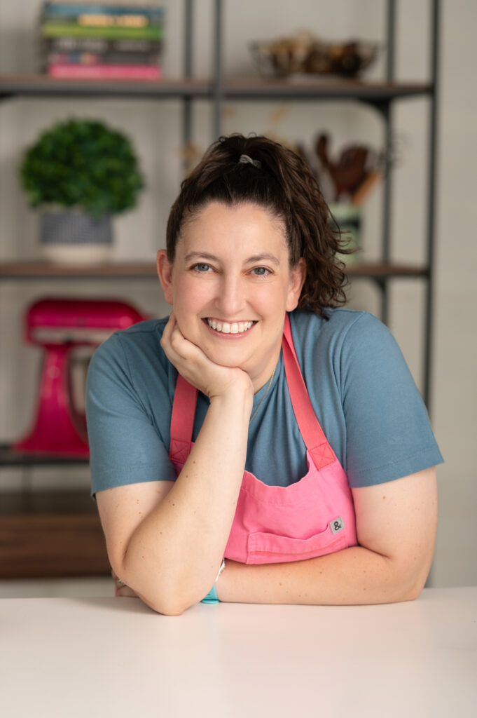 Liz wearing a pink apron leaning on a counter with her chin on her palm.