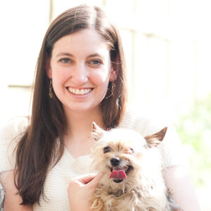A headshot of Liz holding Gizmo, a small Yorkie with his tongue out.