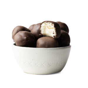 A white bowl filled with mint julep bourbon balls with a bite taken out of one ball showing the filling inside.