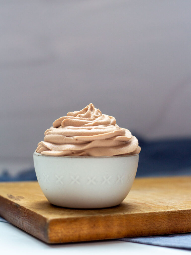 A bowl of Nutella Whipped Cream in a small white bowl on a brown cutting board.