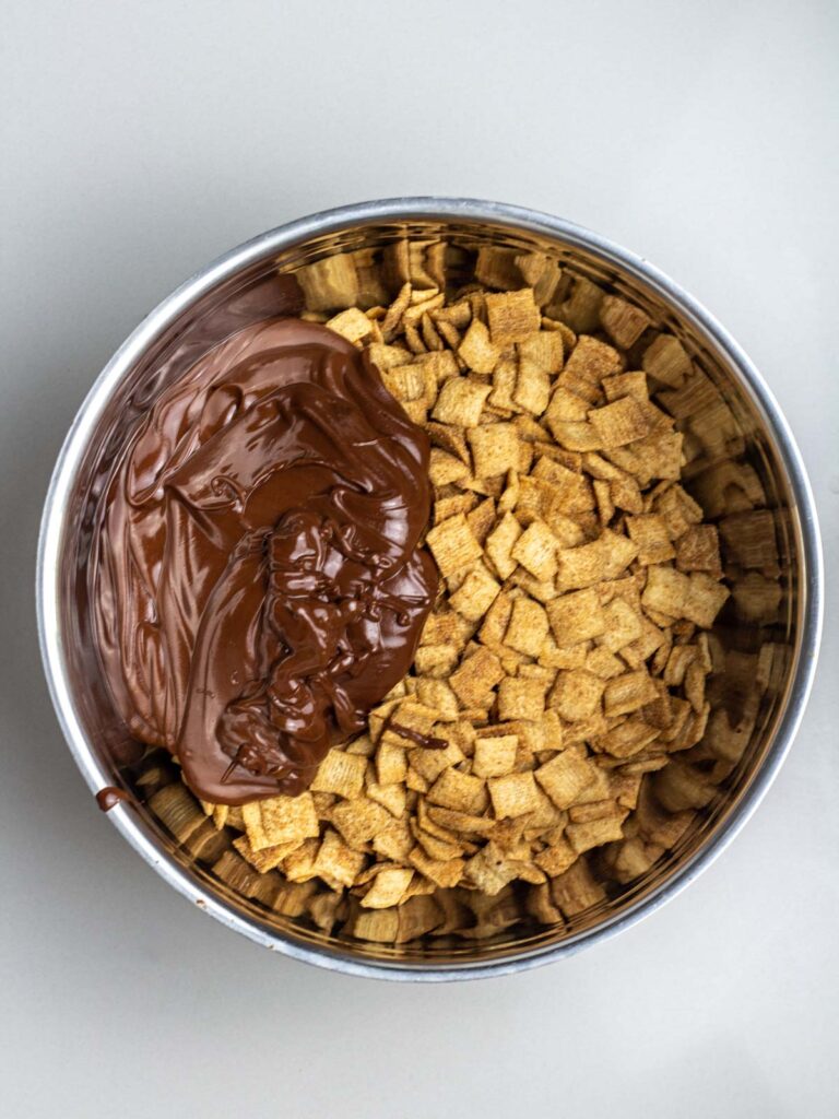 A large mixing bowl filled with cinnamon toast crunch cereal with melted chocolate peanut butter on top.