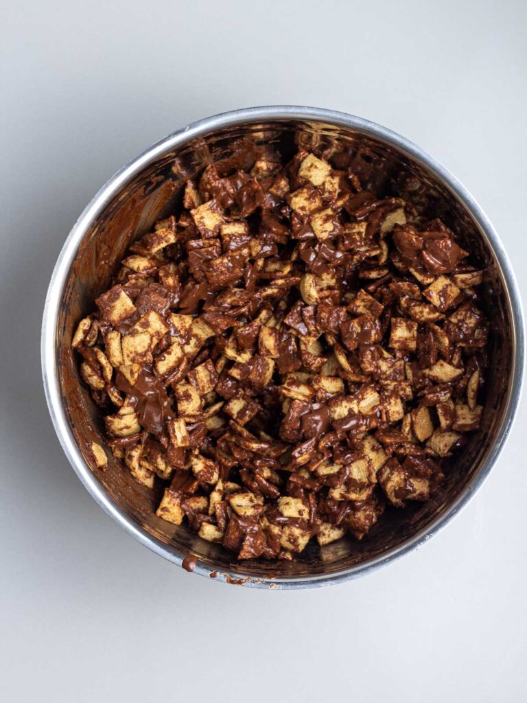 A mixing bowl of cinnamon toast crunch cereal coated in melted chocolate and peanut butter.