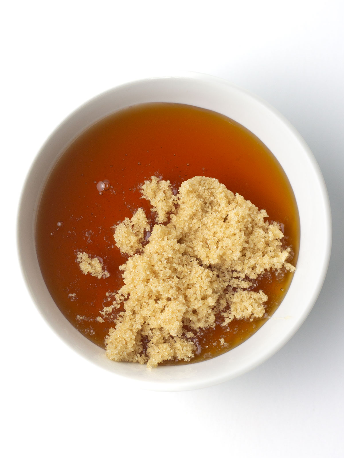 A white bowl of honey with brown sugar on top.