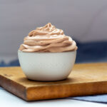 A bowl of Nutella Whipped Cream in a small white bowl on a brown cutting board.