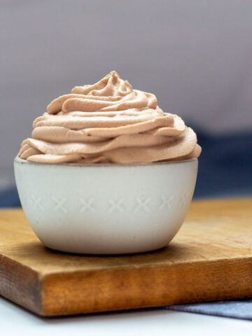 A bowl of Nutella Whipped Cream in a small white bowl on a brown cutting board.