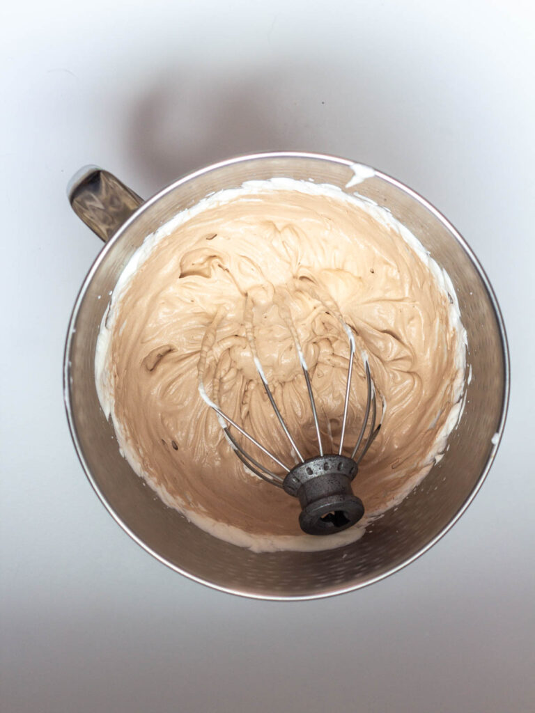 A mixing bowl of Nutella Whipped Cream with a whisk attachment in the whipped cream.