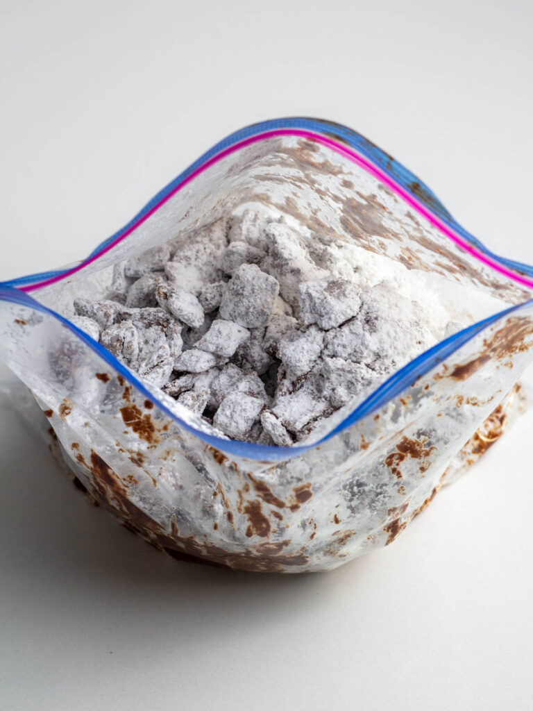 A zip top baggie filled with cinnamon toast crunch puppy chow coated in powdered sugar.