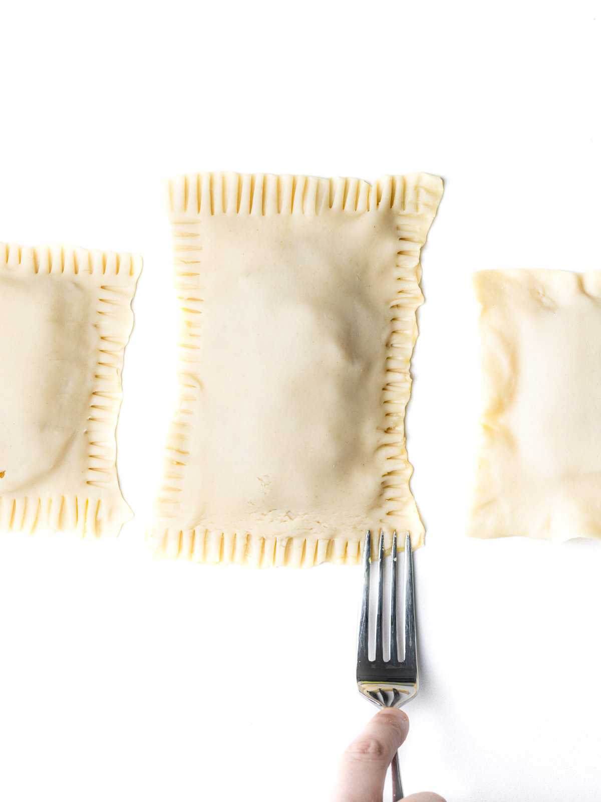 A hand holding a fork to press indentations into the edges of the pop tarts.